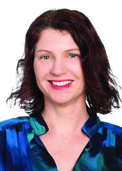 Person, identified as Ms Alison Beasley, wearing a vibrant blue patterned blouse, posed against a plain white background.