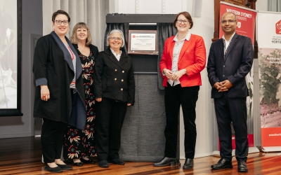 Five formally dressed individuals stand in front of an unveiled plaque mounted on a curtained stand, with a Western Sydney University banner visible to the right.