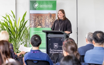 Bonnie Johnson – ARC’s A/g Branch Manager,  Executive and Communications – speaking at a black podium with The University of Queensland’s logo. A banner beside the podium reads “ARC Research Hub for Engineering Plants to Replace Fossil Carbon”.