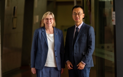 ARC CEO Prof Ute Roessner and Hub Director Distinguished Prof Tianyi Ma standing side by side in a hallway, both wearing formal business suits. The background shows a corridor with muted lighting and glass panels on one side.