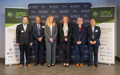 Monash VC and President Prof Sharon Pickering, ARC CEO Prof Ute Roessner and Hub leadership standing in a row in front of a backdrop with Monash University branding. Two banners on either side display the Hub logo and text about forging a greener future for a low-carbon steel industry.