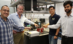Image: David Marpaung, Benjamin Eggleton, Yang Liu and Amol Choudhary inside the Sydney Nanoscience Hub, pointing at a thumbnail-size chip being evaluated in the broadband microwave testbed.