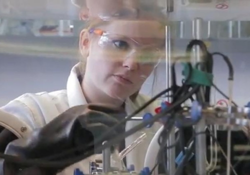 woman working on device in the lab wearing coat, gloves and glasses