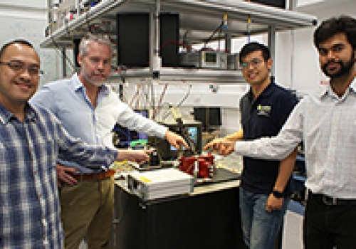 Image: David Marpaung, Benjamin Eggleton, Yang Liu and Amol Choudhary inside the Sydney Nanoscience Hub, pointing at a thumbnail-size chip being evaluated in the broadband microwave testbed.