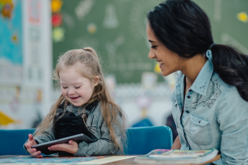 Child with Down syndrome using a tablet in a classroom with teacher. iStock, FatCamera.jpg