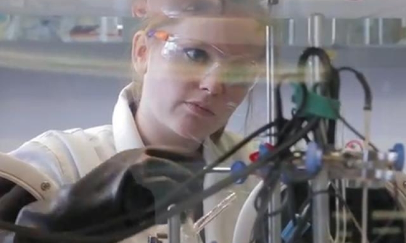 woman working on device in the lab wearing coat, gloves and glasses
