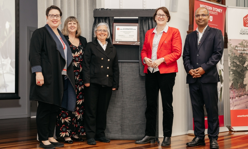 Five formally dressed individuals stand in front of an unveiled plaque mounted on a curtained stand, with a Western Sydney University banner visible to the right.