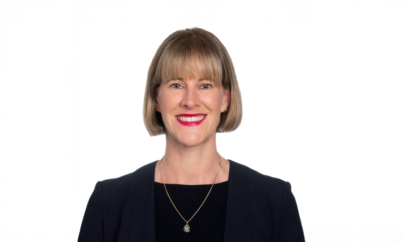 Person, identified as Ms Claire Forsyth, wearing a dark blazer over a light top, accessorised with a pendant necklace, posed against a plain white background.