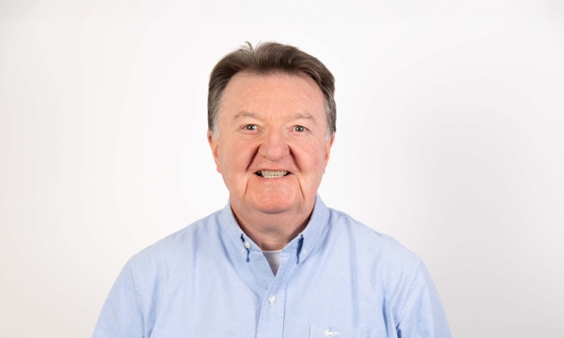 Person, identified as Prof Alastair McEwan, wearing a light blue button-up shirt with a small embroidered logo, posed against a plain white background