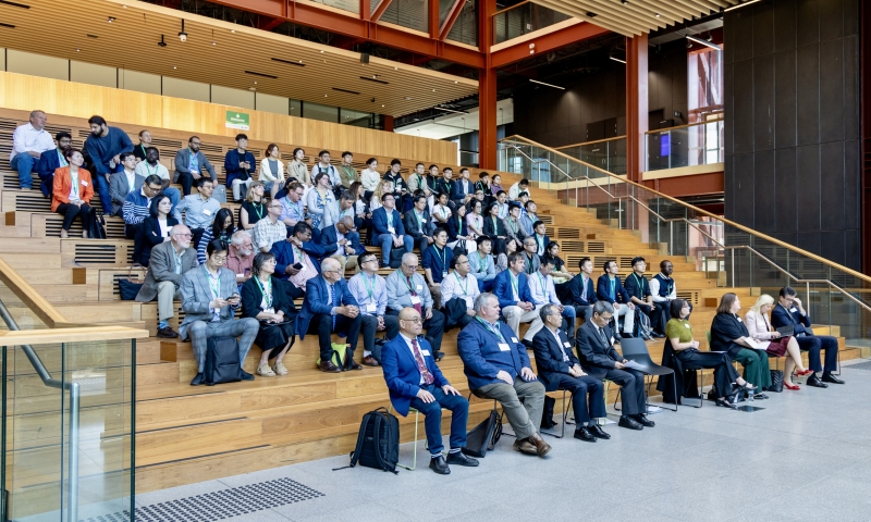 Attendees sit on a large set of wooden stairs, facing a speaker.