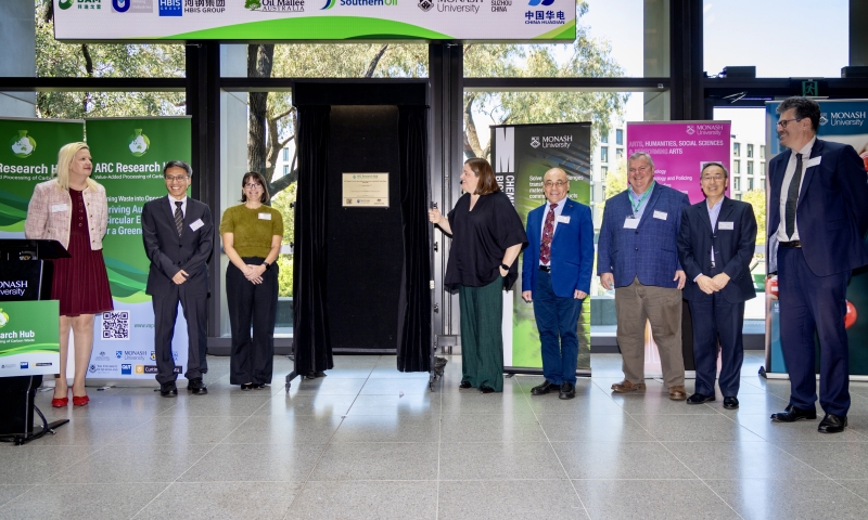 9 people standing in front of large windows, unveiling the plaque to officially launch the Research Hub. From left to right are Professor Katya Pas, Prof Lian Zhang, Ms Helen Partridge, Ms Bonnie Johnson, Prof Dongke Zhang, Mr Bert Huys, Prof Geoff Wang and Professor Yiannis Ventikos. 