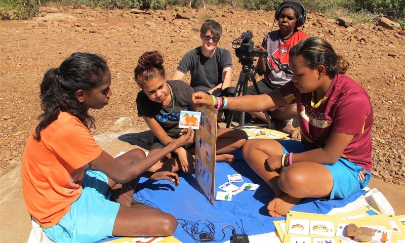 A group sits outdoors using illustrated cards and recording equipment during an activity.