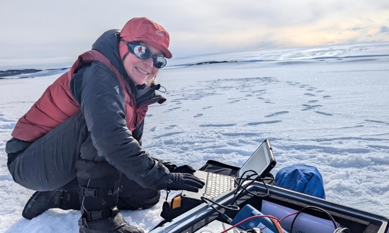 Prof Reading in winter gear uses a laptop and scientific instruments on a snowy landscape.
