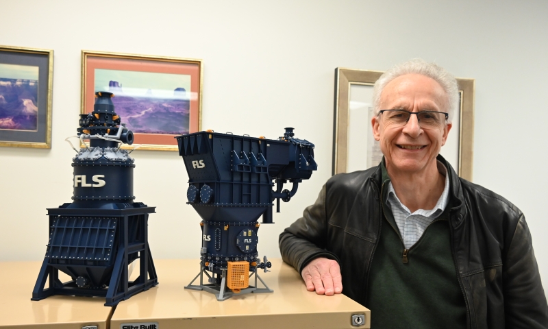 Laureate Professor Kevin Galvin standing beside two scale models of industrial mining equipment displayed on a cabinet in an office setting, with framed landscape photographs in the background.